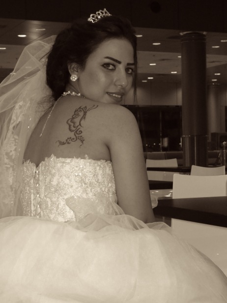 An Egyptian Bride waits for her new husband at the Kuwait airport, fully dressed in white wedding gown and veil. Here she shows off her butterfly tattoo