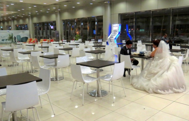 An Egyptian Bride waits for her new husband at the Kuwait airport, fully dressed in white wedding gown and veil. Here, her groom made an appearance. The two met with a sincere kiss and settled down to exchange stories. In the airport cafe.