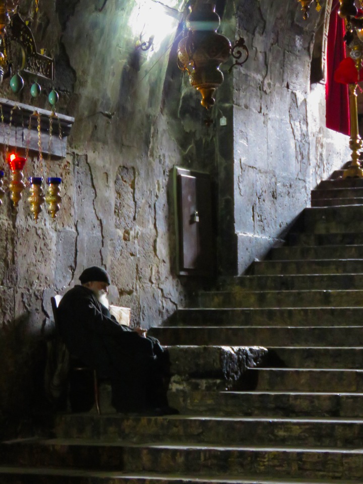 A priest waits on the steps of Church of the Sepulchre of Saint Mary in Jerusalem Israel - by Anika Mikkelson - Miss Maps - www.MissMaps.com